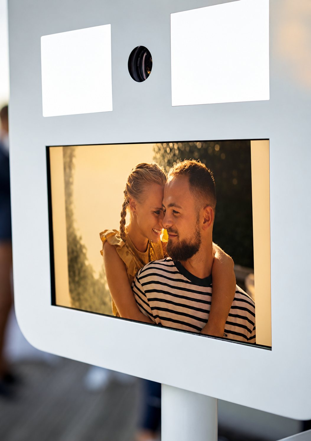 Gros plan sur une borne photo blanche dont l'écran affiche une photo d'un homme et d'une femme souriants, front contre front.